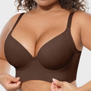 May include: A brown bra with adjustable straps and underwire support. The bra has a longline design, extending down the torso. The fabric appears smooth and seamless, with a subtle sheen. The bra is being held at the bottom edge.
