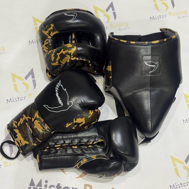 Puede incluir: Un conjunto de equipo de boxeo negro, que incluye un protector de cabeza, un protector facial y guantes. Los guantes y el casco presentan un patr&oacute;n de camuflaje en tonos marrones y verdes. Cada pieza tiene un logotipo de paloma blanca.