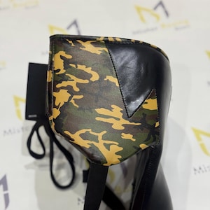 Puede incluir: Bota negra con un estampado de camuflaje en la parte superior. El dise&ntilde;o de camuflaje presenta tonos de verde, marr&oacute;n y amarillo. La bota tiene un dise&ntilde;o elegante y moderno.