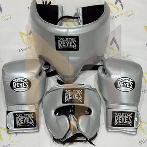 May include: A set of silver boxing equipment including two boxing gloves, a headgear, and a groin protector. Each piece features a black and white Cleto Reyes logo patch. The items are constructed with a metallic silver finish and black straps.