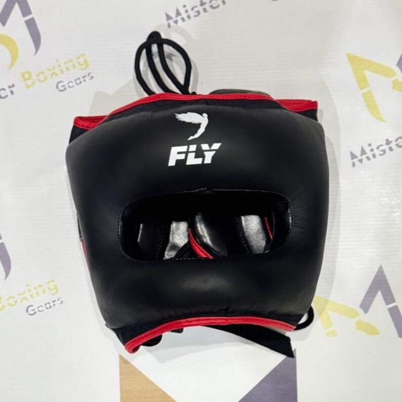May include: Black boxing headgear with red trim. The headgear has a large opening for the face and smaller openings for the ears. The word "FLY" is printed in white on the front, along with a white graphic of a bird. A black cord is attached to the top.