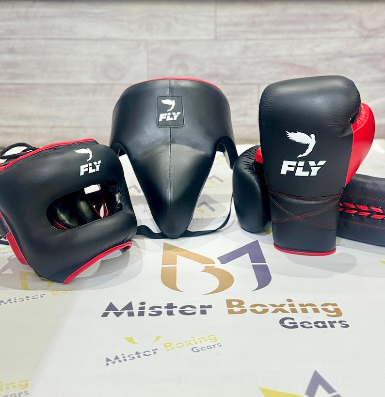 May include: A boxing gear set featuring a black headgear, a face protector, and boxing gloves with red accents. The gloves and headgear have the word "FLY" and a bird logo. The set is designed for protection during training and matches.