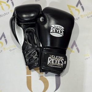 以下が含まれることがあります： 白いアクセントが入った黒いCleto Reyesボクシンググローブのペア。グローブの手首ストラップと手の甲にはCleto Reyesのロゴがあり、手首ストラップには「HECHO EN MEXICO」および「PROFESIONAL」という文字がプリントされています。