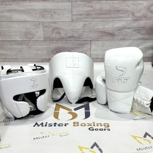 May include: White boxing gear set including a head guard, a pair of gloves, and a face protector. Each piece has the word "FLY" and a logo printed on it. The set is displayed on a white surface with the text "Mister Boxing Gears".