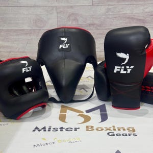 May include: Black boxing headgear, gloves, and groin protector with red trim. Each piece has the white "FLY" logo. The gloves and headgear are on the left and the groin protector is in the center. The gloves are red and black.