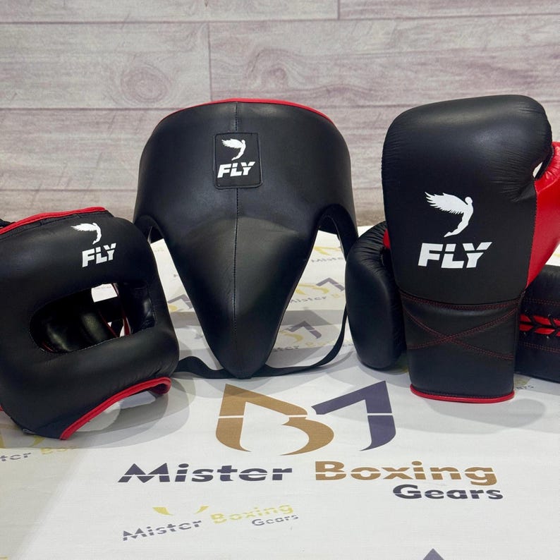 May include: Black boxing headgear, gloves, and groin protector with red trim. Each piece has the white "FLY" logo. The gloves and headgear are on the left and the groin protector is in the center. The gloves are red and black.