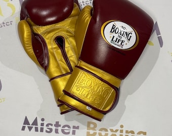 Op de afbeelding: Een paar boks handschoenen in bordeauxrood en goud. De handschoenen hebben de tekst "NO BOXING NO LIFE" op de polsband en de achterkant. De handschoenen zijn gemaakt van leer en hebben een gewatteerd ontwerp.