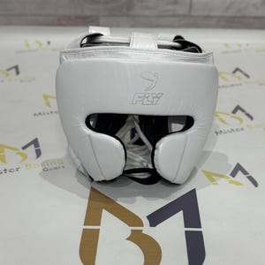 May include: A white boxing headgear with the word "FLY" printed on the front. The headgear has a padded design with openings for the eyes, ears, and mouth. The headgear is designed to protect the head during boxing or other combat sports.