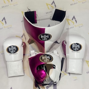 Op de afbeelding: Een boksset bestaande uit twee witte en magentakleurige bokshandschoenen, een bijpassende hoofdbeschermer en een tok. Elk onderdeel is voorzien van een zwart ovaal embleem met de tekst No Boxing No Life en Hecho en Mexico. De uitrusting heeft een tweekleurig ontwerp.