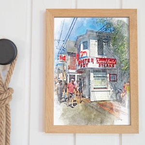 May include: A framed watercolor print of a restaurant with the text "Lobster Boy" and "Charcoal Broiled Steaks". The print is in a light wood frame and hangs on a white wall. A black hook with a rope knot is to the left.