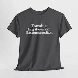 Peut inclure: T-shirt gris foncé avec le texte blanc : « Pour faire court, je suis devenu éditeur ». Le t-shirt a des manches courtes et un col rond. Le texte est centré sur le devant du vêtement.