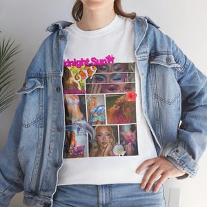 Op de afbeelding: Wit T-shirt met een collage van afbeeldingen en de tekst "Midnight Sun" in roze en geel. De collage bevat afbeeldingen van een vrouw, een dolfijn en een bloem. Het shirt wordt gedragen met een blauw spijkerjasje.