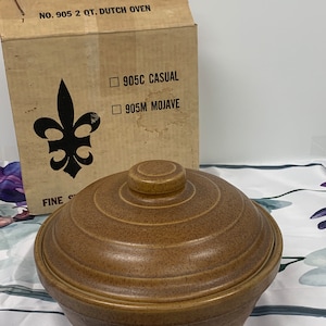 May include: A 2 quart brown ceramic Dutch oven with a lid. The box says "NO. 905 2 QT. DUTCH OVEN" and has a fleur-de-lis logo. The box also says "905C CASUAL" and "905M MOJAVE".