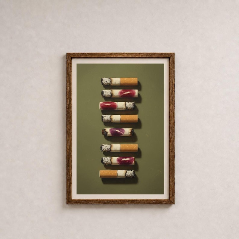 A framed art print featuring a vertical stack of used cigarettes with lipstick marks on a green background.