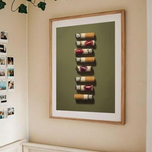 The framed lipstick cigarettes print hanging on a beige wall above a bed decorated with artificial ivy.