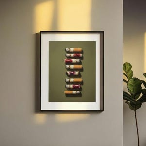 A black-framed print of the lipstick cigarettes artwork hanging on a grey wall with warm sunlight washing over it.