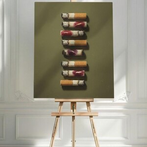 The lipstick cigarettes art print displayed on a wooden easel in a bright white room.
