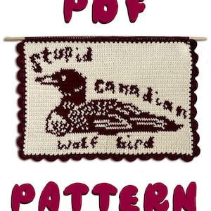 May include: A cream-colored crochet pattern featuring a dark red loon design with the words "stupid Canadian wolf bird". The pattern is framed with a dark red scalloped edge and includes the text "PDF PATTERN".