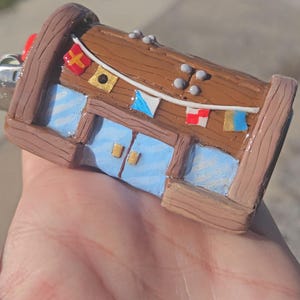 May include: A miniature, handcrafted replica of a building, featuring a brown exterior with blue window panels and decorative flags. The model has a whimsical design, with a red element on the side.