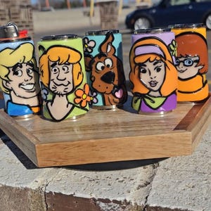 May include: Five novelty lighters, each decorated with a different cartoon character. The lighters are brightly coloured and feature detailed artwork of characters from a popular animated series. They are presented on a wooden tray.