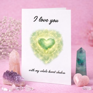 May include: A white greeting card with the text "I love you" and "with my whole heart chakra". The card features a green heart design. The card is surrounded by crystals in shades of pink, purple, and green.
