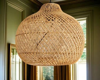 May include: A large, woven rattan pendant light. The light has a bulbous shape with a wide, open base and a narrower top. The natural tan colour of the rattan creates a warm glow. The fixture hangs from a black cord, suitable for a living room or dining area.