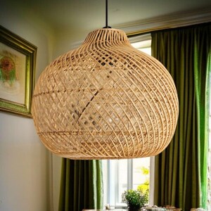 May include: A woven rattan pendant light. The light has a bulbous shape with a wide base and a narrower top. It is suspended from a black cord and is made of natural-coloured rattan.