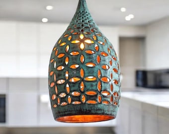 Op de afbeelding: Een tealkleurige hanglamp met een druppelvorm en ingewikkelde bloemvormige uitsparingen. De lamp hangt aan een dun snoer en straalt een warme, oranje gloed uit. Het ontwerp is een decoratief element voor de verlichting van het huis.