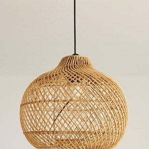 May include: A woven rattan pendant light. The light has a rounded, bell-shaped shade in a natural tan colour. The shade is suspended from a black cord. The light fixture is designed to be hung from the ceiling.