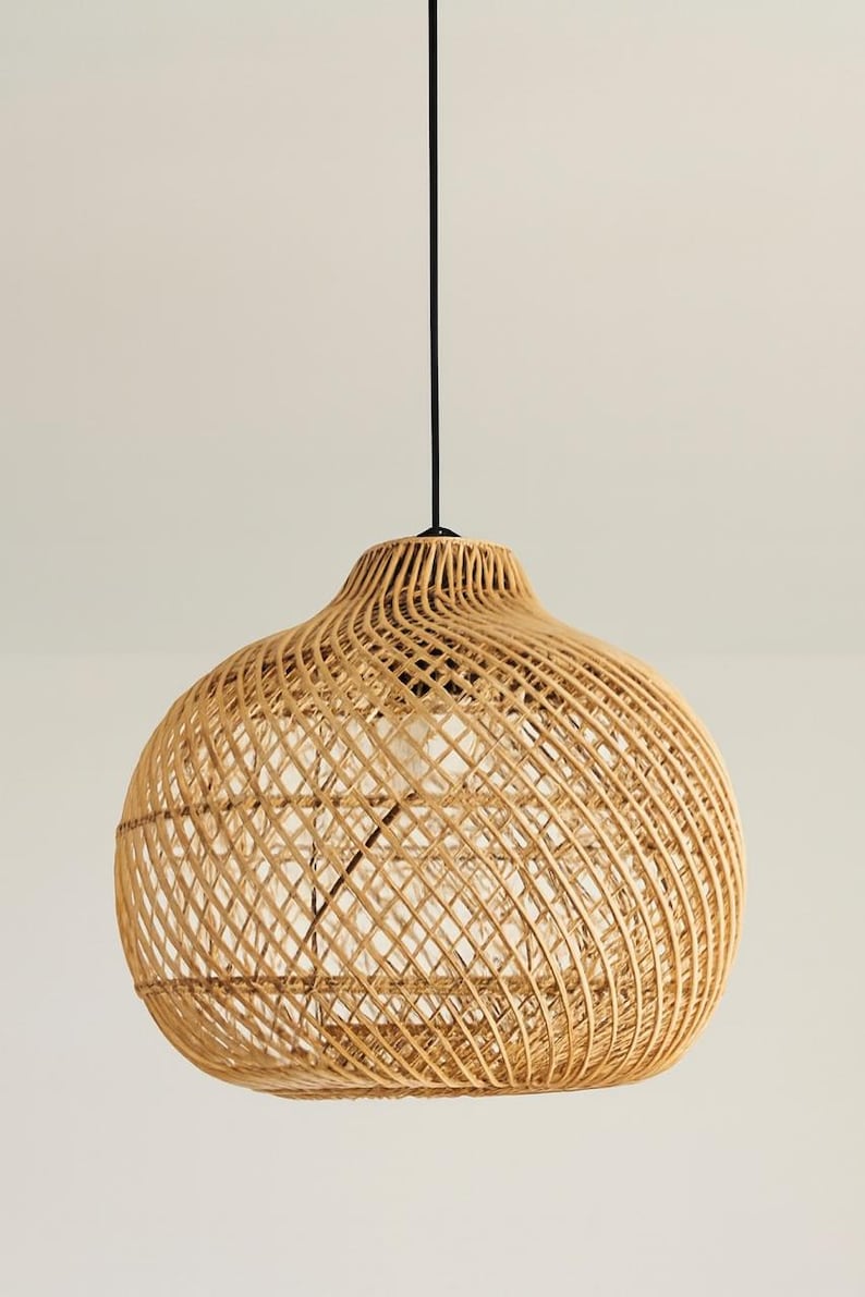 May include: A woven rattan pendant light. The light has a rounded, bell-shaped shade in a natural tan colour. The shade is suspended from a black cord. The light fixture is designed to be hung from the ceiling.