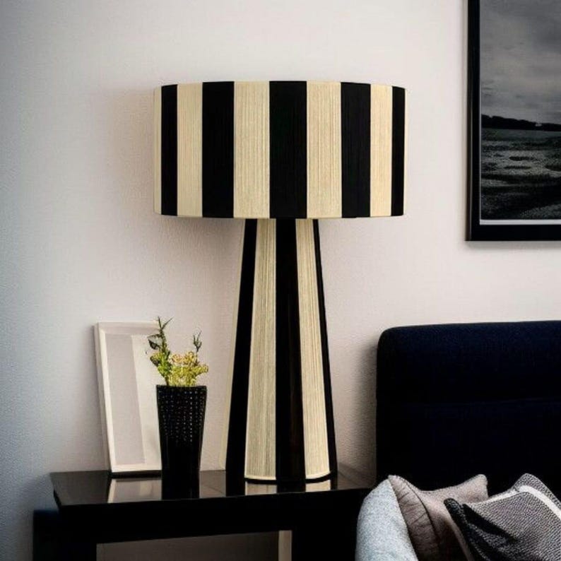 May include: A black and cream striped table lamp with a cylindrical shade and a matching base. The lamp is on a black table with a black vase and a framed picture. The lamp's height is approximately 24 inches.