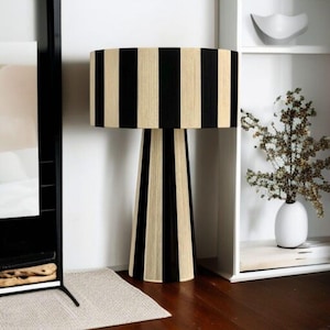 May include: A striking lamp with a cylindrical shade and a conical base, featuring a black and beige striped pattern. This decorative lighting fixture would be a stylish addition to a living room or bedroom. The lamp's design is modern and eye-catching.