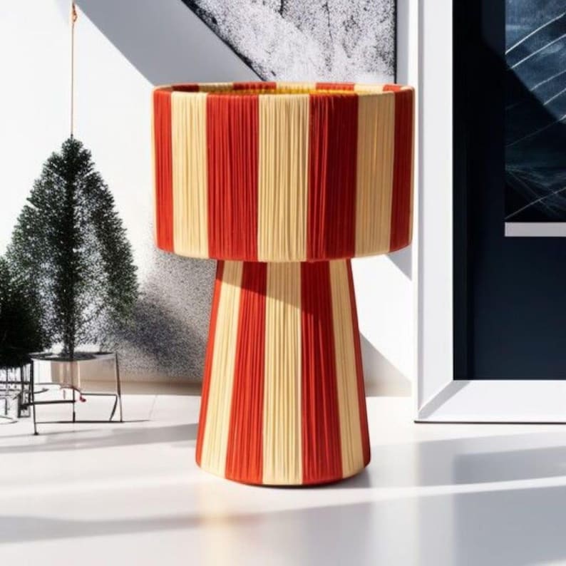 May include: A decorative lamp with a cylindrical shade and a pedestal base. The lamp features vertical stripes in alternating red and cream colors. The lamp is a unique home decor item.