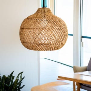 May include: A woven rattan pendant light. The light fitting is a natural tan colour and has a round, bulbous shape. The light hangs from a black cord and is suspended in a bright room.