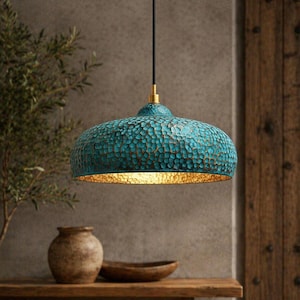 May include: A teal-coloured, textured pendant light with a gold-coloured interior. The light fixture hangs from a black cord with a gold-coloured accent. The light has a hammered metal appearance and is dome-shaped.