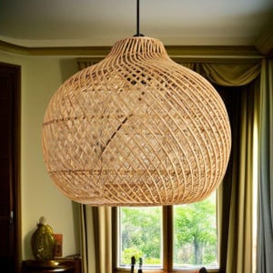 May include: A large, woven rattan pendant light. The light has a spherical shape with a wide base and a narrower top, suspended from a black cord. The natural beige colour of the rattan creates a warm, inviting aesthetic, suitable for interior decor.