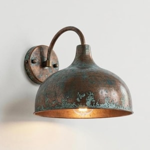 May include: A wall-mounted light fitting with a copper-coloured finish. The fixture has a domed shade with a distressed effect, a curved arm, and a circular mounting plate. The light bulb is visible inside the shade, and the design has a vintage feel.