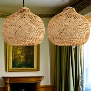 May include: Two spherical pendant lights made from woven rattan hang from the ceiling. The light fittings have a woven pattern. The lights are suspended by black cords. The background includes a painting and green curtains.