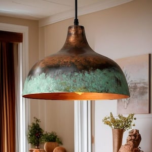 May include: A large, dome-shaped pendant light fixture with a copper finish. The fixture has a dark brown top, transitioning to a green-blue patina, and a warm orange interior. The light hangs from a black cord, illuminating the space below.
