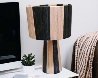 Può includere: Lampada da tavolo decorativa con paralume e base a righe nere e beige. Il design presenta strisce verticali. La lampada è su un tavolo bianco. È visibile una piccola pianta in vaso.
