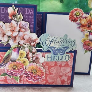 May include: A handmade card with a purple, pink, and green floral design. The card features a hummingbird, a butterfly, and the text "Fluttering by to say Hello".