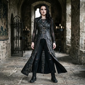 Könnte beinhalten: Ein langer, schwarzer Ledermantel mit mehreren Schnallen und Taschen. Der Mantel wird über einem schwarzen Mesh-Top und schwarzen Jeans mit zerrissenen Knien getragen. Das Outfit wird durch schwarze Stiefel vervollständigt. Der Hintergrund ist ein Steinflur mit gewölbten Decken.