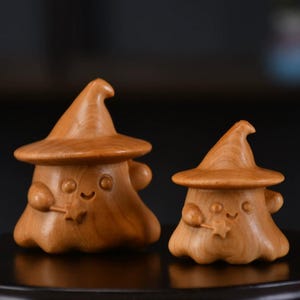 Puede incluir: Dos figuras de madera con forma de hongo, cada una con un sombrero puntiagudo. Las figuras tienen caras sonrientes y sostienen pequeñas varitas con puntas en forma de estrella. La madera tiene un tono cálido y natural.