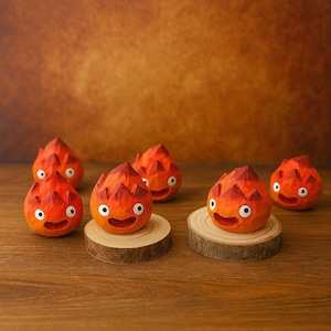 May include: Six orange, flame-shaped wooden figurines with smiling faces and white eyes. The figurines are arranged on a wooden surface, some placed on small wooden slices. The background is a warm, brown tone.