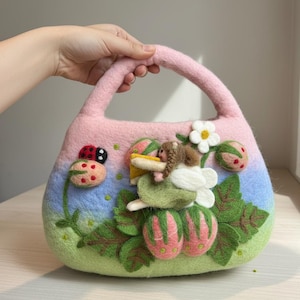 May include: A felted handbag with a pink handle and body, decorated with a ladybug, strawberries, and a fairy. The bag features a gradient of pink, blue, and green colors, with white flower accents and green leaves.