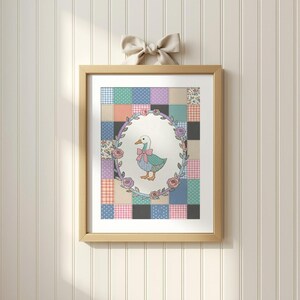 May include: A framed print featuring a charming illustration of a duck wearing a pink bow, set against a patchwork quilt background. The artwork is enclosed in an oval frame adorned with floral accents, and the frame is made of light wood.