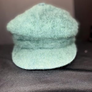 May include: A seafoam green newsboy cap with a rounded crown and a small, stiff brim. The hat has a textured, fuzzy appearance. The cap is made of a soft material and is suitable for casual wear.