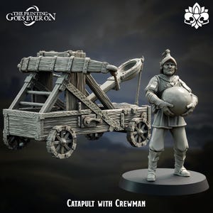 Może przedstawiać: Miniaturowa szara katapulta ze szczegółowym drewnianym wzorem, z kołami i mechanizmem wyrzutni. W pobliżu stoi pasująca szara figurka członka załogi trzymającego dużą kulę. Tekst "CATAPULT WITH CREWMAN" znajduje się na dole.