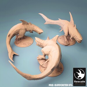 May include: Three beige shark-like sculptures with detailed features, including fins, teeth, and tails, are displayed on circular bases. The sculptures are arranged against a light blue background. The text "PRE-SUPPORTED STL" and a logo are visible.
