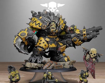 Op de afbeelding: Een grote, gepantserde ork-miniatuur geschilderd in geel en zwart, met een massieve mechanische klauw en een zwaar kanon. Het wordt vergezeld door drie kleinere groene goblin-figuren, waarvan er één een gescheurde rode banier met een schedel draagt.